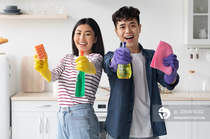 Cheerful asian couple with supplies for cleaning posing in kitchen