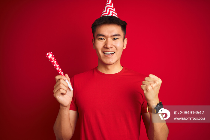 Asian chinese man on birthday celebration wearing funny hat over isolated red background screaming p