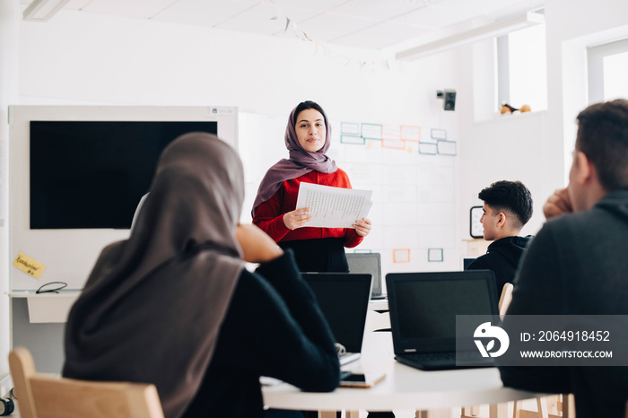 Teenage girl giving presentation to students at classroom in university