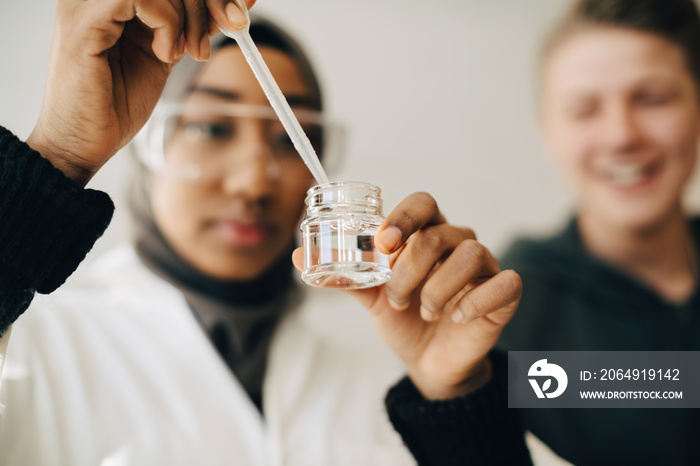 Close-up of teenage students mixing solution during scientific experiment in chemistry class