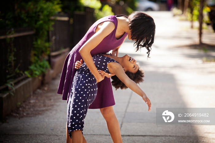 Young woman dancing with daughter (8-9) on sidewalk