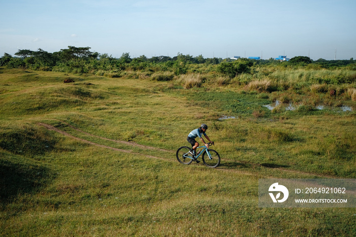 A young bearded cyclist is biking through a field