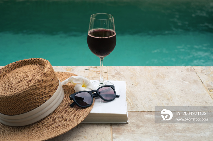 游泳池边的棕色巴拿马帽和一杯红酒。夏季旅行概念