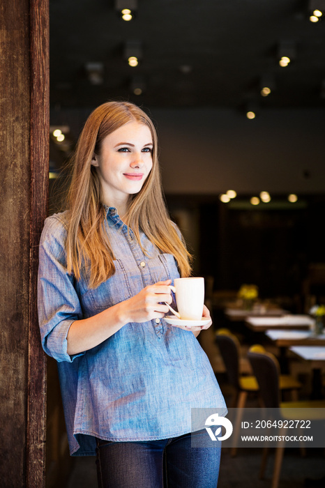 Smiling young woman with coffee cup standing in cafe