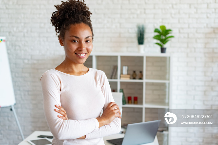 Charming woman in office, folded arms and smiling looking at the camera leaned the table