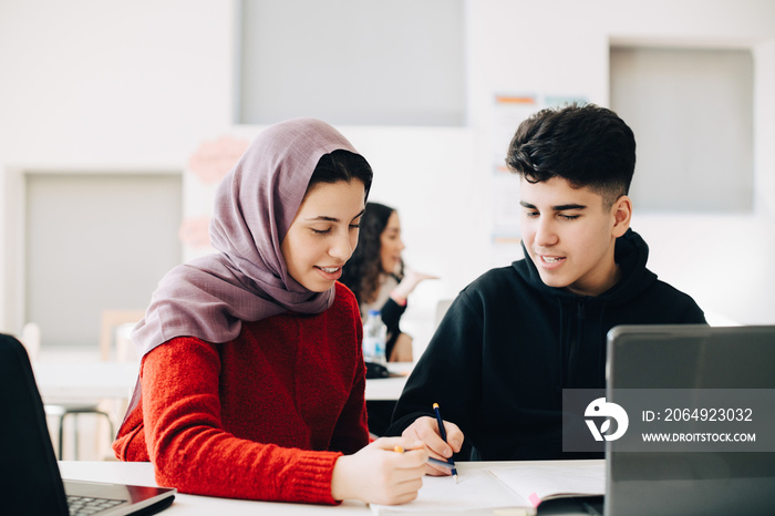 Male and female students discussing together while studying in classroom