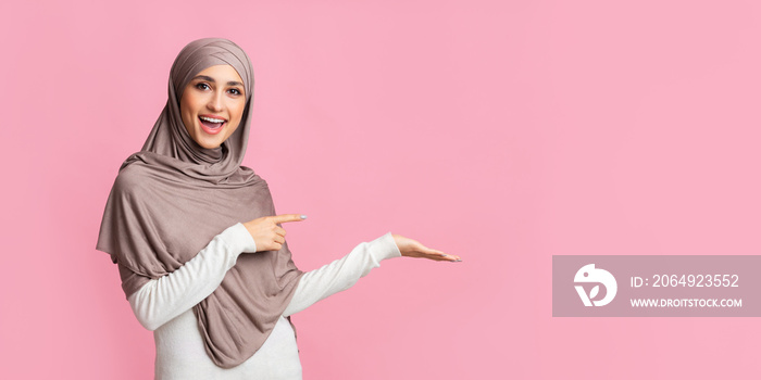 Beautiful girl in hijab pointing at something on her empty palm