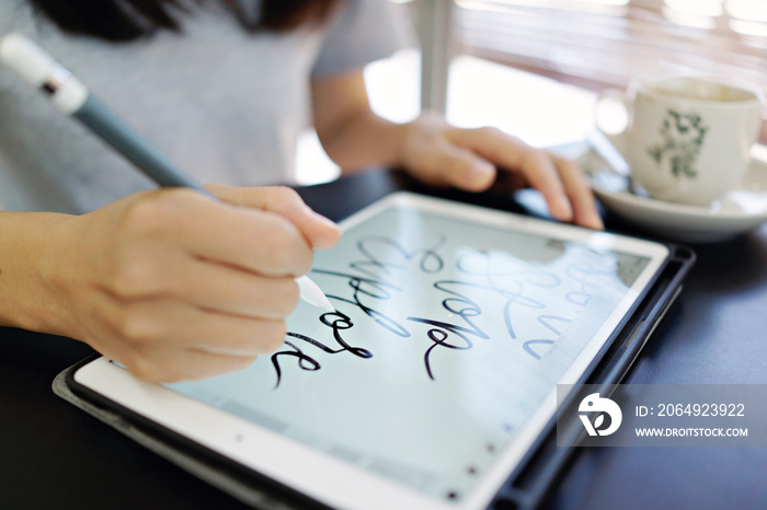 一名女性使用苹果铅笔在iPad上使用Procreate应用程序手写字母。