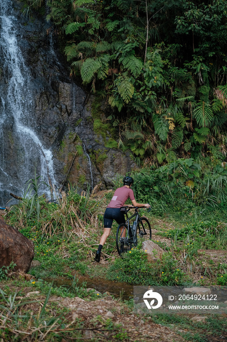 A young female cyclist is carrying her bike to look at the waterfalls.