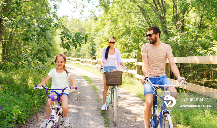 family, leisure and people concept - happy mother, father and little daughter with bicycles in summe