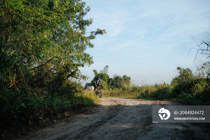 A young bearded cyclist is biking through a dirt path.