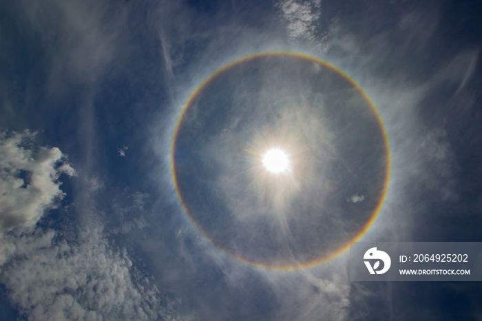 circular rainbow halo around the sun among blue sky and white clouds.