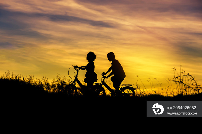 剪影小男孩和小女孩在日落时骑自行车玩得很开心