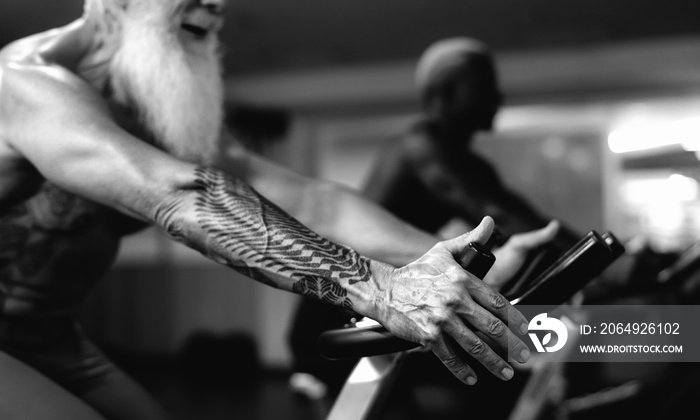 Senior and young men doing bike exercises in gym - People with different age and race training on cy