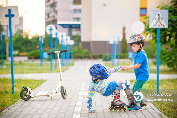 two boys in park, help boy with roller skates to stand up