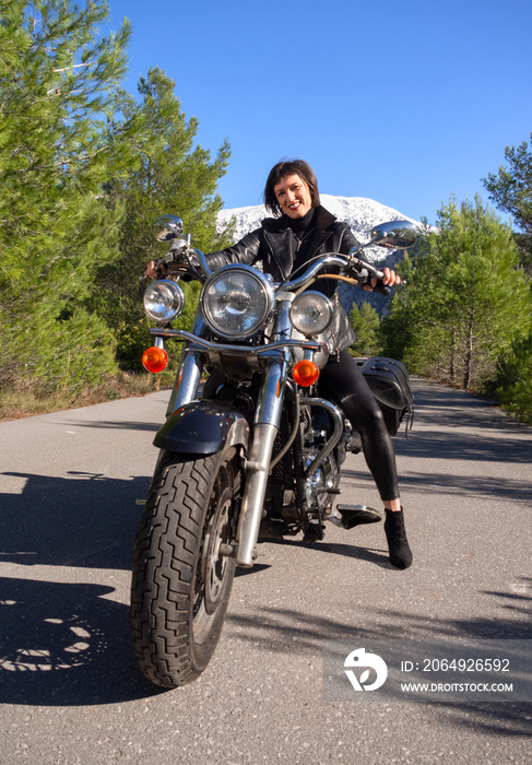 一名身穿黑色皮夹克的女子在希腊森林中的一条路上骑着一辆斩波摩托车。