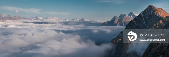 Mountain panorama, snowy peaks above thick clouds against a blue sky