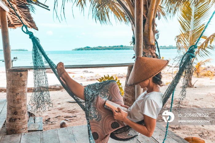 Woman reading book on hammock tropical beach, real people getting away from it all, traditional sout