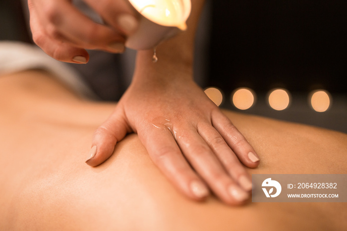 beauty, wellness and bodycare concept - close up of woman having back massage with hot oil candle at