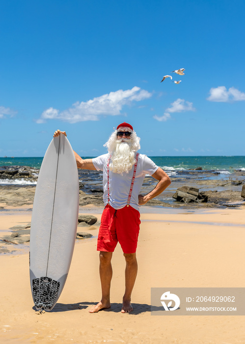 Santa Claus with a surf board with the ocean on backgraund. Australia, Christmas in summer time.