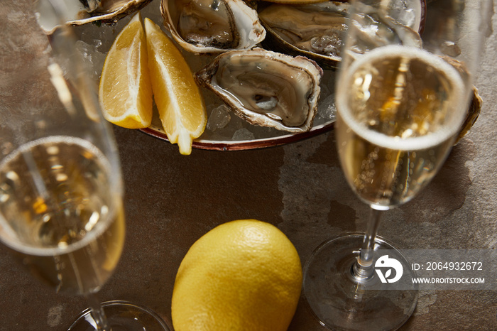 selective focus of oysters and lemons in bowl with ice near champagne glasses with sparkling wine