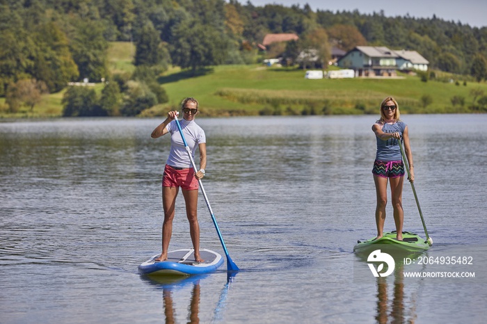 两名女性在斯洛文尼亚的Smartinsko湖中骑着立式桨板