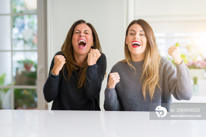 Beautiful family of mother and daughter together at home very happy and excited doing winner gesture