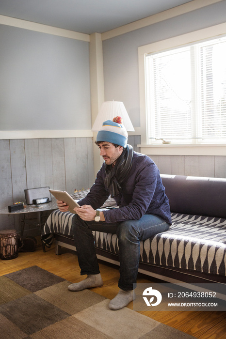 Man wearing hat sitting on sofa and looking at tablet