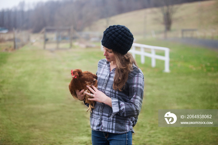 Young woman in plaid shirt holding chicken