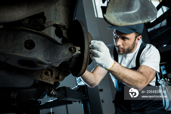 selective focus of auto mechanic in cap and gloves repairing automobile in car service