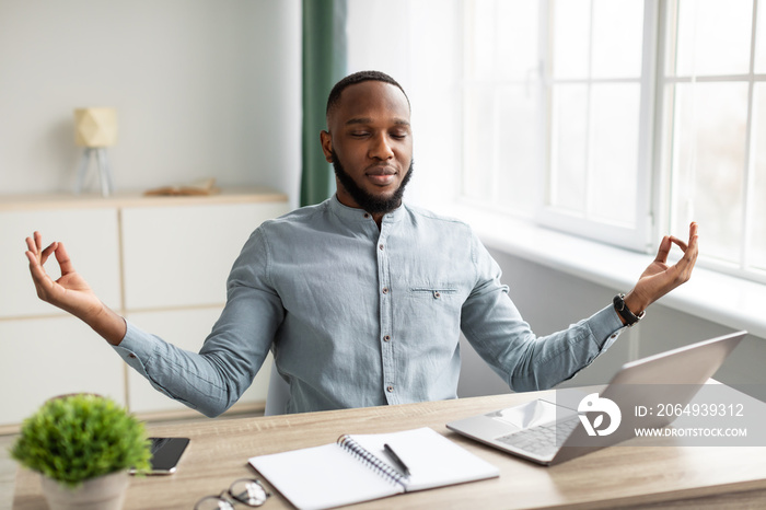 Peaceful African Businessman Meditating Sitting At Workplace Relaxing In Office