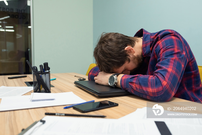 Overworked tired manager sleeping on the desk after a hard day at work. Tired man falls asleep in th