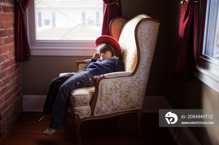 Little boy (4-5) sitting in armchair by window