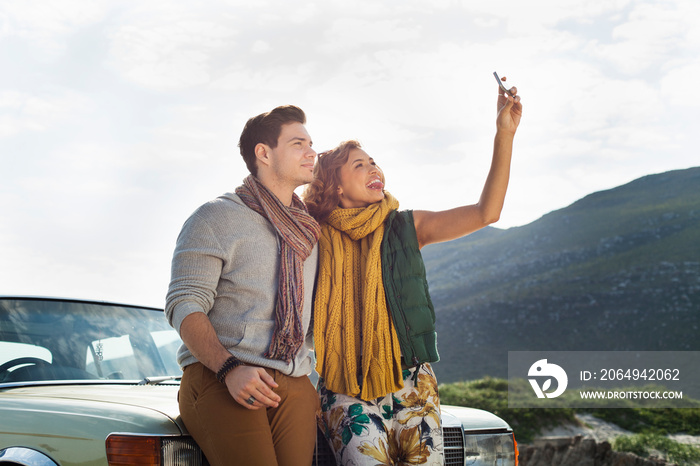 Young couple leaning against car taking selfie on smartphone, Cape Town, Western Cape, South Africa