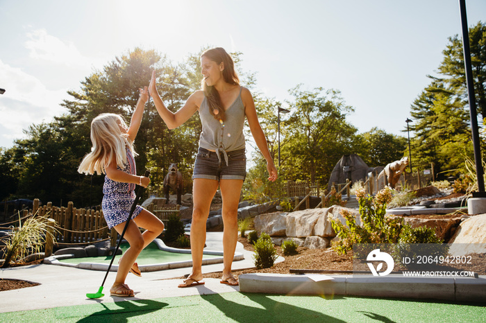 Happy daughter giving high-five to mother after scoring at miniature golf course