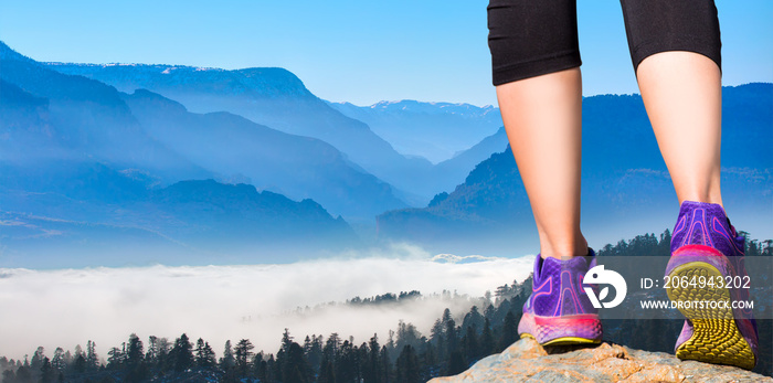 穿着运动鞋的女性双脚站在蓝山白云中的岩石上的特写——女性行走