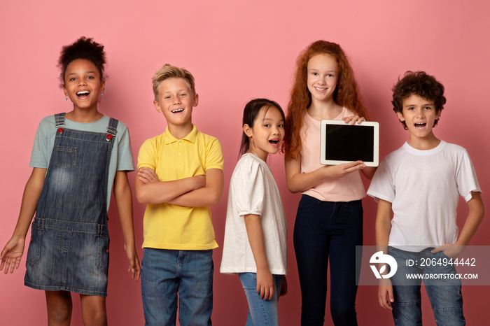 快乐的多元化学童拿着粉色背景的空屏幕平板电脑，实物模型