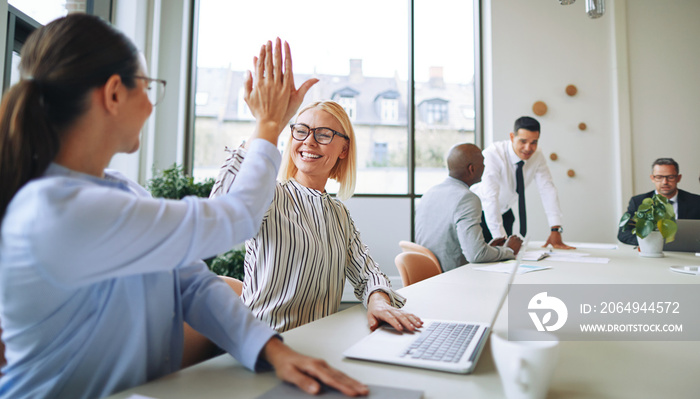 Two smiling young businesswomen high fiving together in a boardr