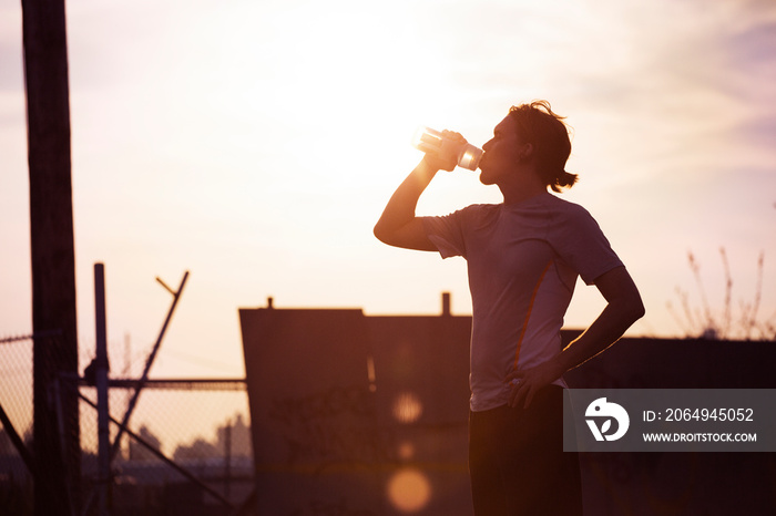 Man drinking water while standing against clear sky at sunrise