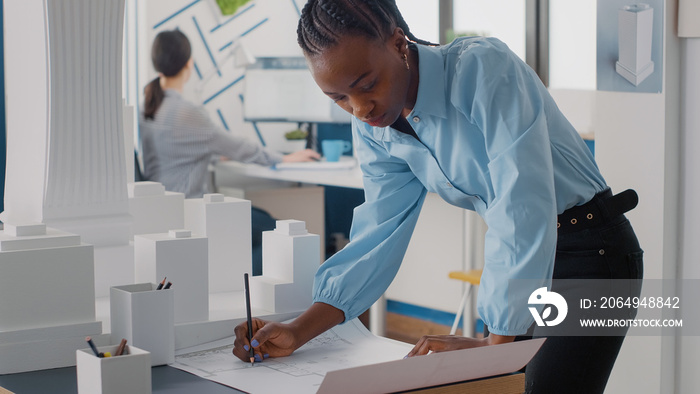 Engineer working on blueprints plans on desk to design building model and maquette. Woman architect 