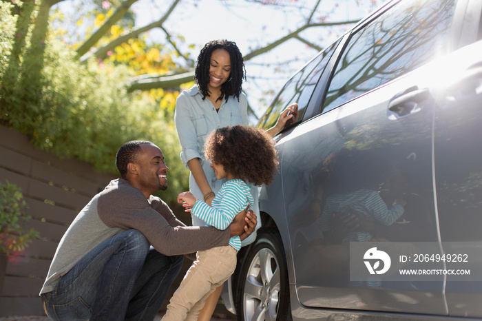 Happy family standing outside car in sunny driveway