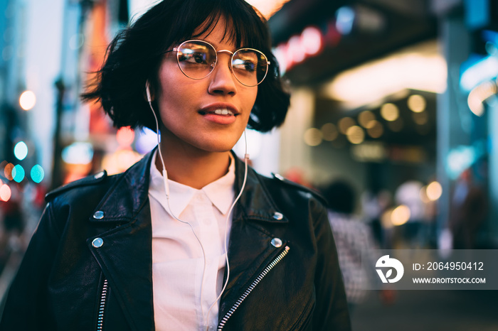 Millennial woman in fashionable clothing listening audio book during evening walk in New York City, 