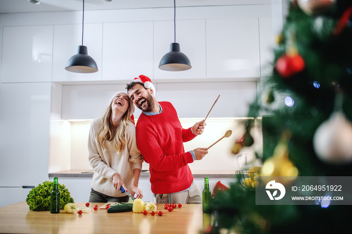 一对戴着圣诞老人帽的快乐白人夫妇站在厨房里准备晚餐
