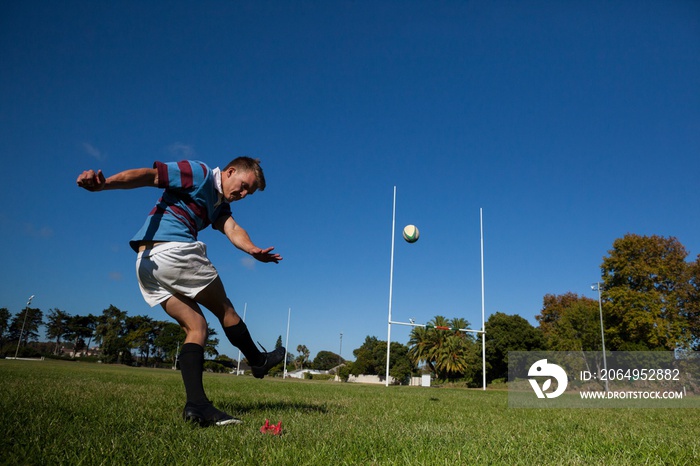 Rugby player kicking ball for goal against clear blue sky