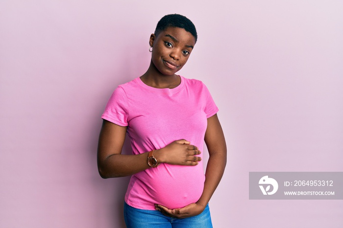 Young african american woman expecting a baby, touching pregnant belly relaxed with serious expressi