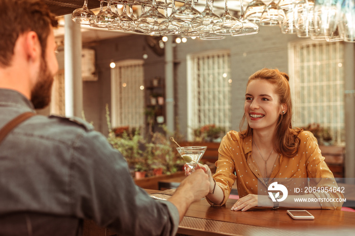 Smiling female taking a martini cocktail from a bartender