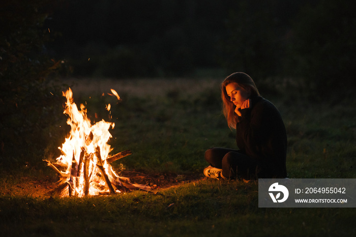 孤独的年轻女子坐在篝火旁取暖。年轻女孩独自一人