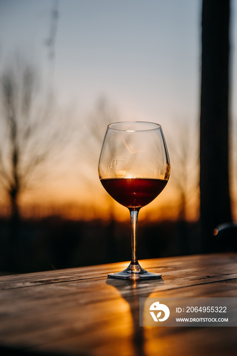 Glass of red wine on a wooden table outdoors in sunset light.