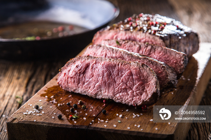 Beef steak. Juicy medium Rib Eye steak slices on wooden board with fork and knife herbs spices and s