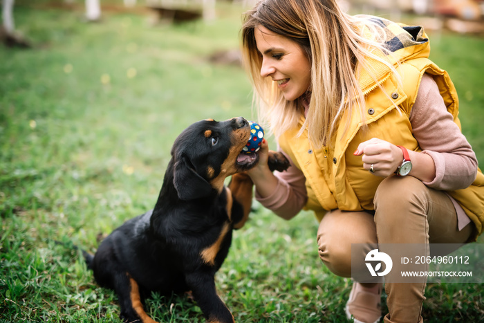 Young woman training and playing with puppy on grass, in park. Rottweiler dog puppy details